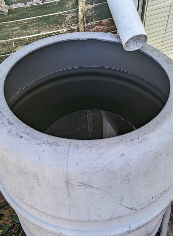 Water tub with a white downpipe allowing water to flow into a open container. The container is filled with dirty looking rainwater